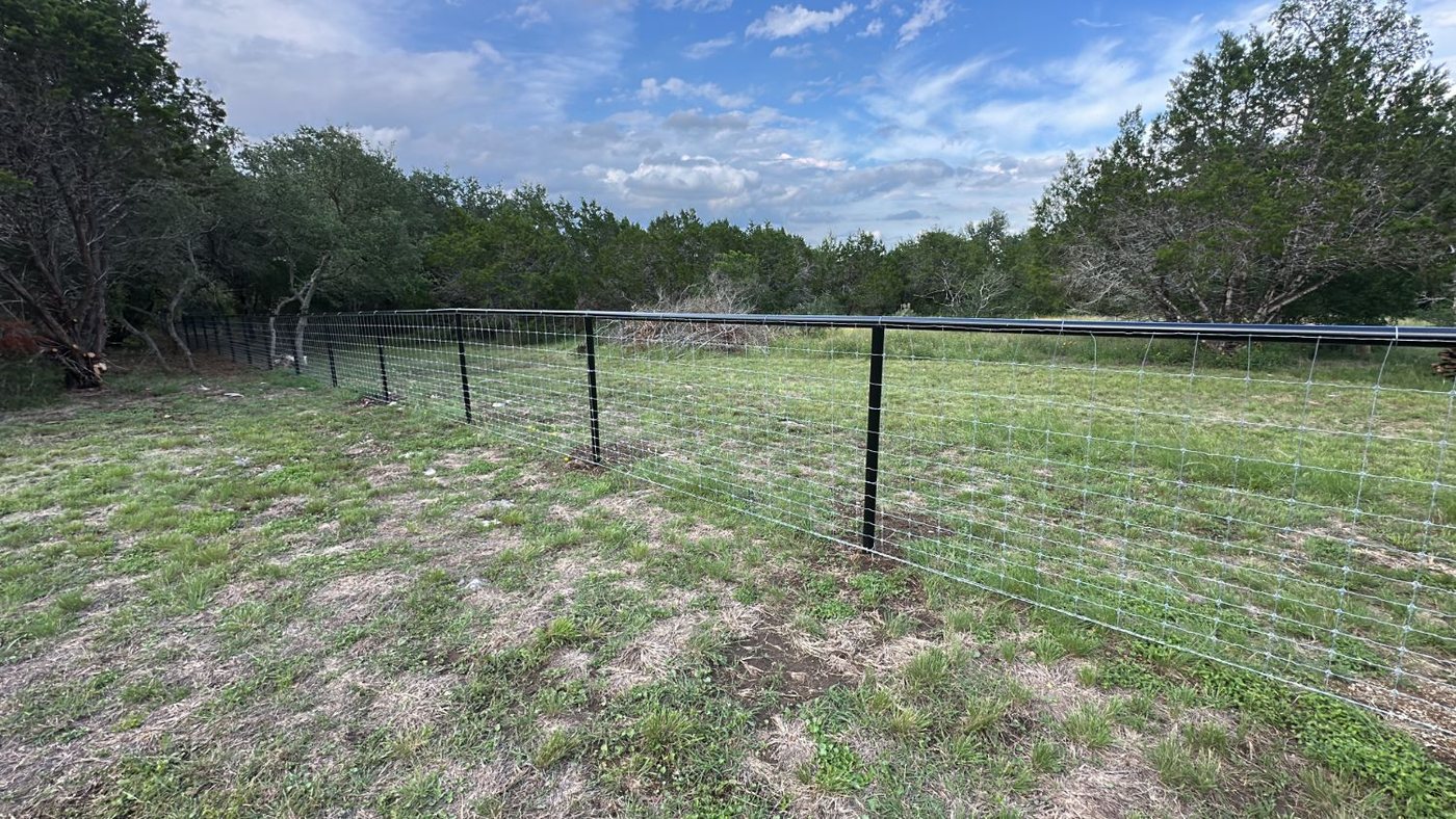 Wire fence on black steel posts with a black pipe top rail, running across open pasture