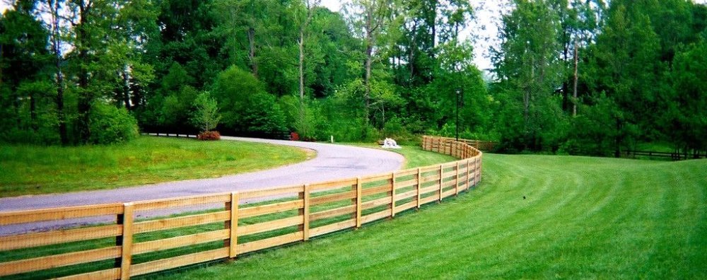 Four-board wood fence curving along a paved drive and mown lawn