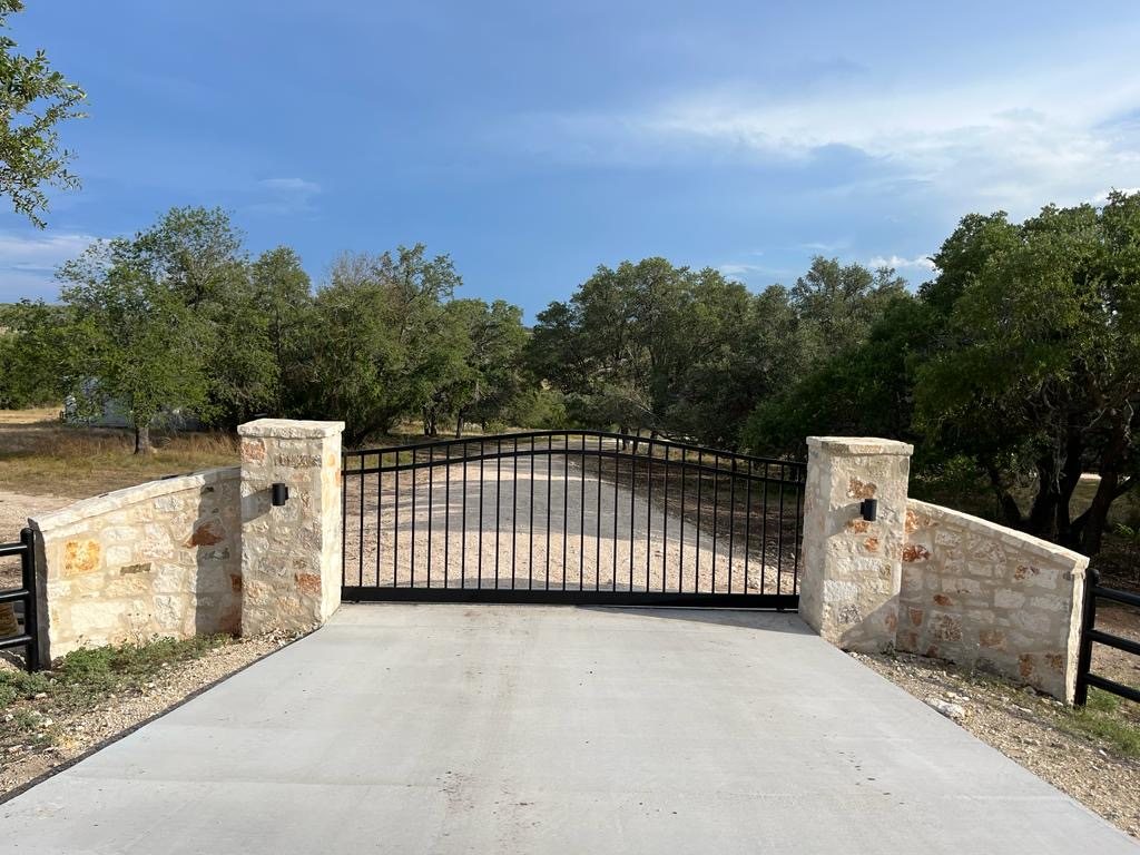 Black arched gate between two limestone columns, with curved stone walls and a concrete apron