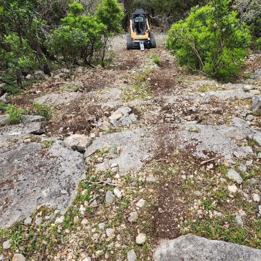 Skid steer clearing brush off a rocky slope