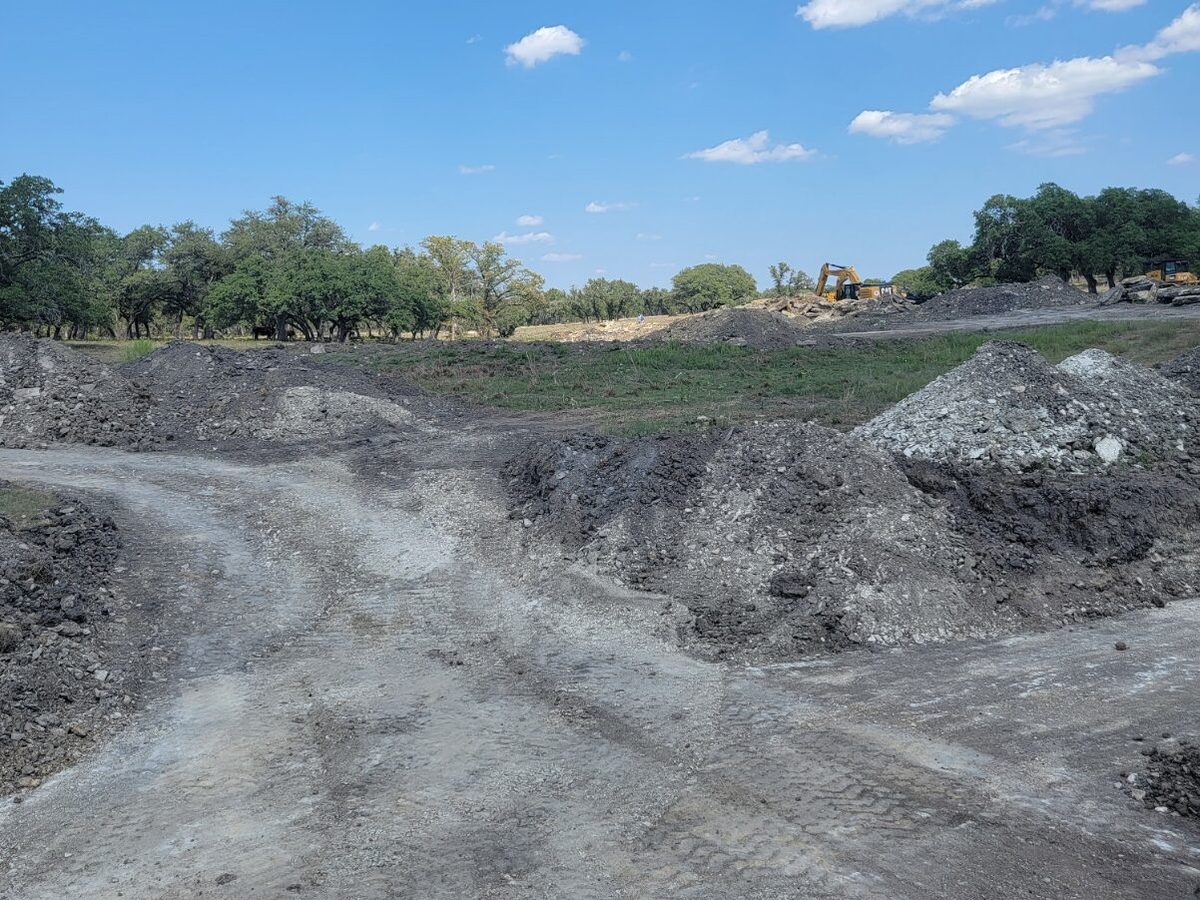 Dug basin of gray soil with spoil piles and equipment tracks