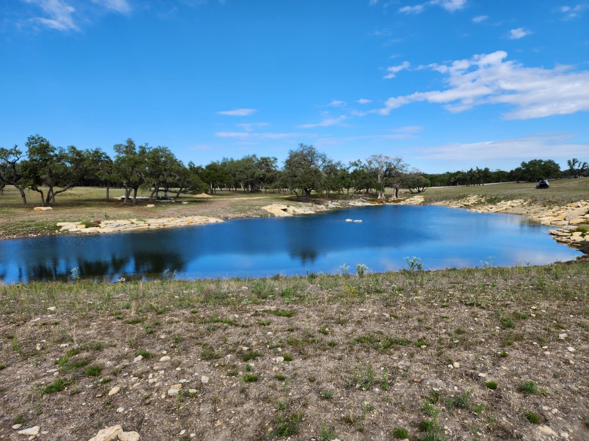 Pond with blue water, a rocky bank and oaks along the far shore