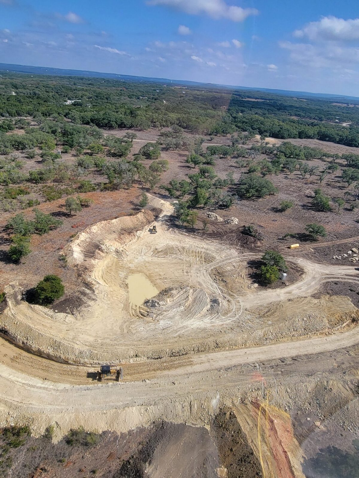 Aerial view of a pond being dug, with a machine on the haul road at the bottom of the frame and another at the top of the basin