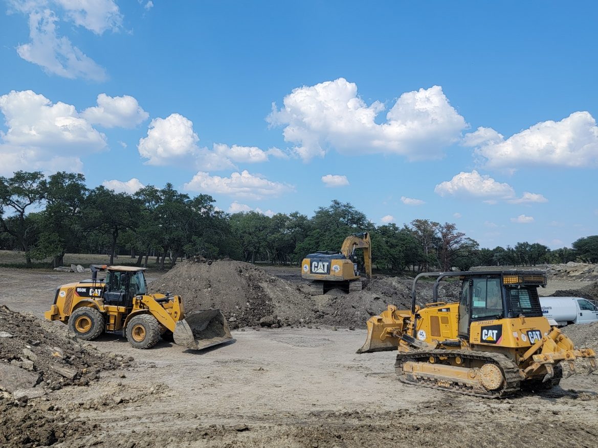 Wheel loader and dozer working on bare ground beside a pond site