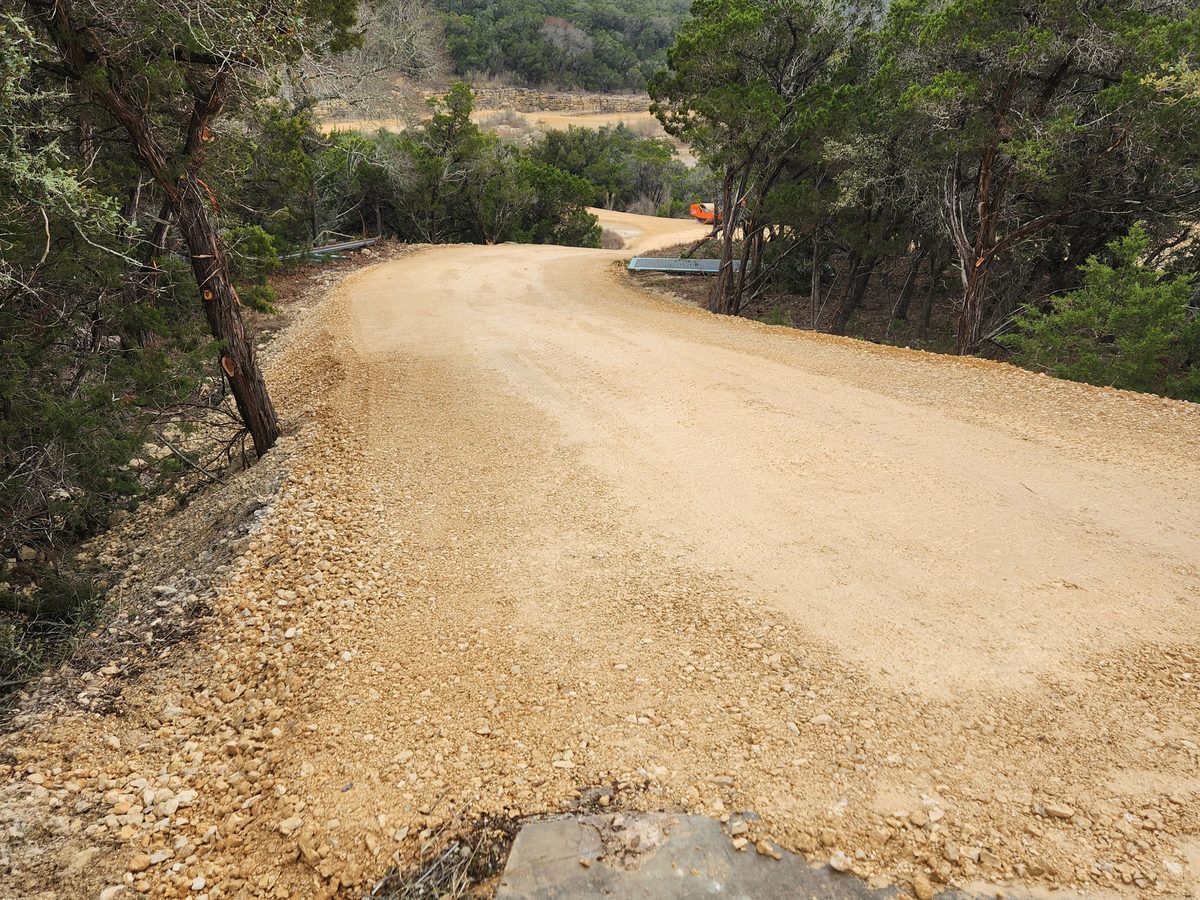 Tan caliche road curving away from a flat rock ledge at the edge of the frame